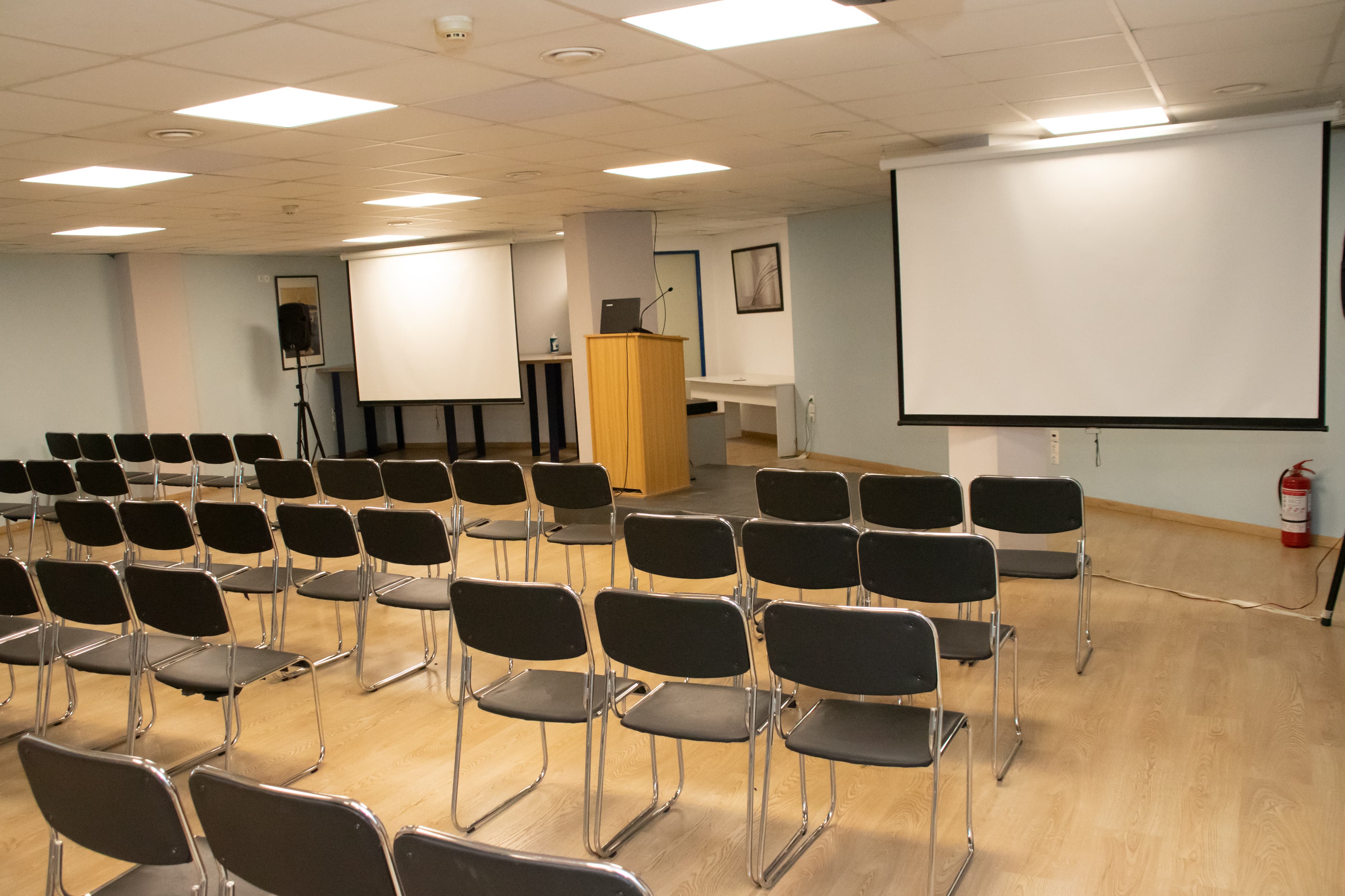 Presentation room with screen and podium, featuring several rows of chairs for attendees