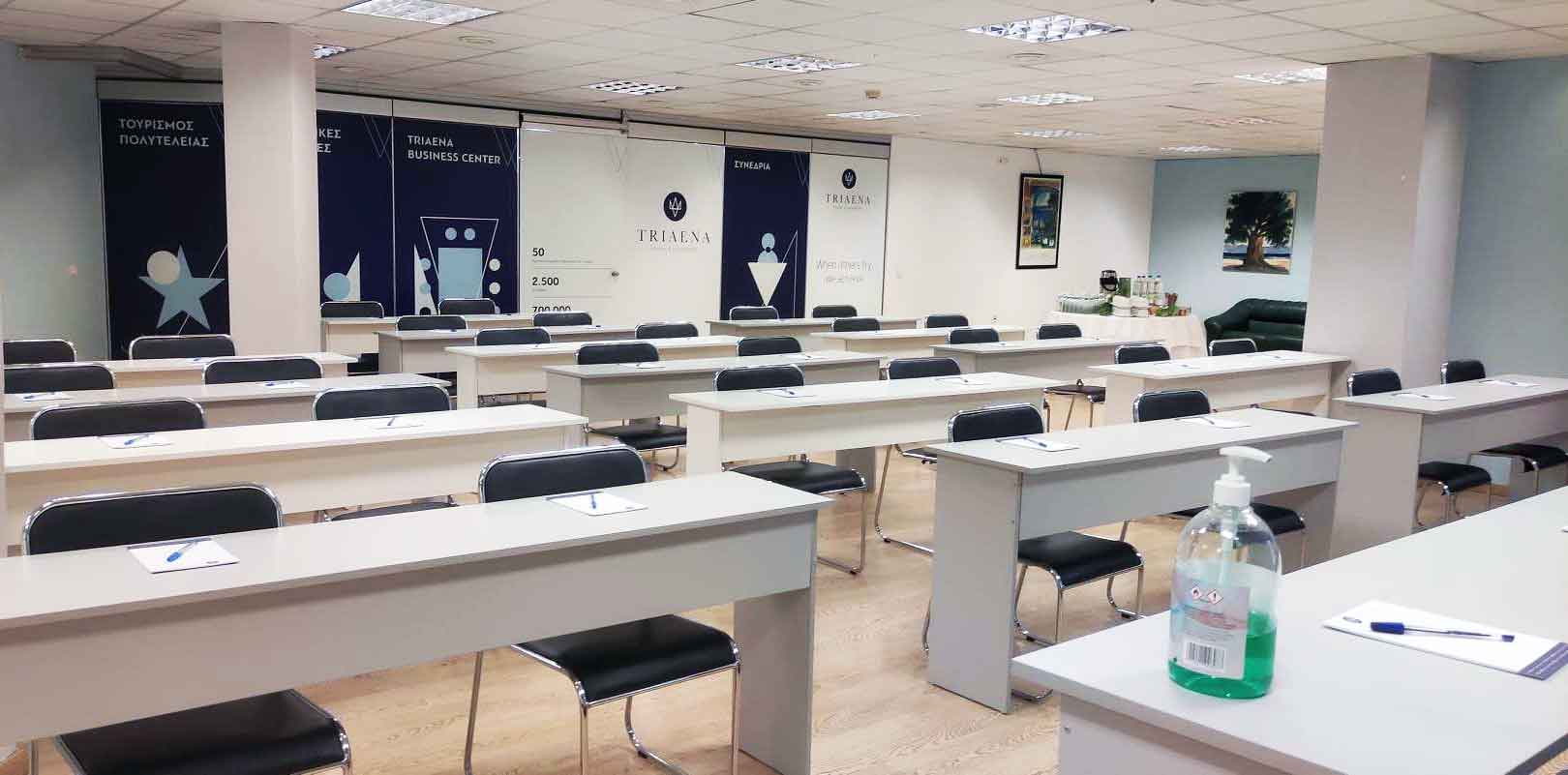 Meeting hall with long white tables and black chairs arranged in rows, suitable for conferences or seminars