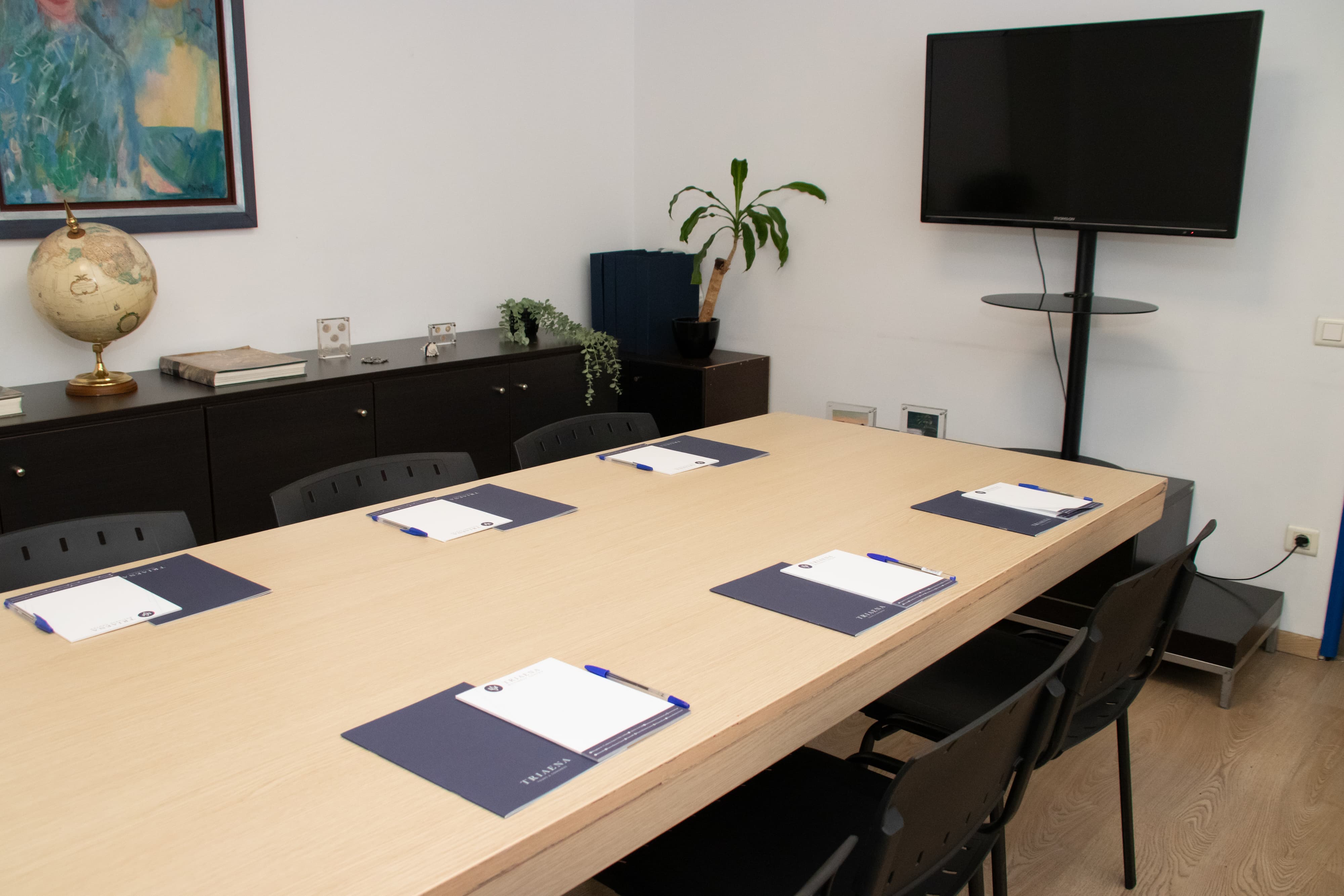 Meeting room with rectangular table setup, notepads and pens at each seat, flat-screen TV, and cabinets with decorative items.