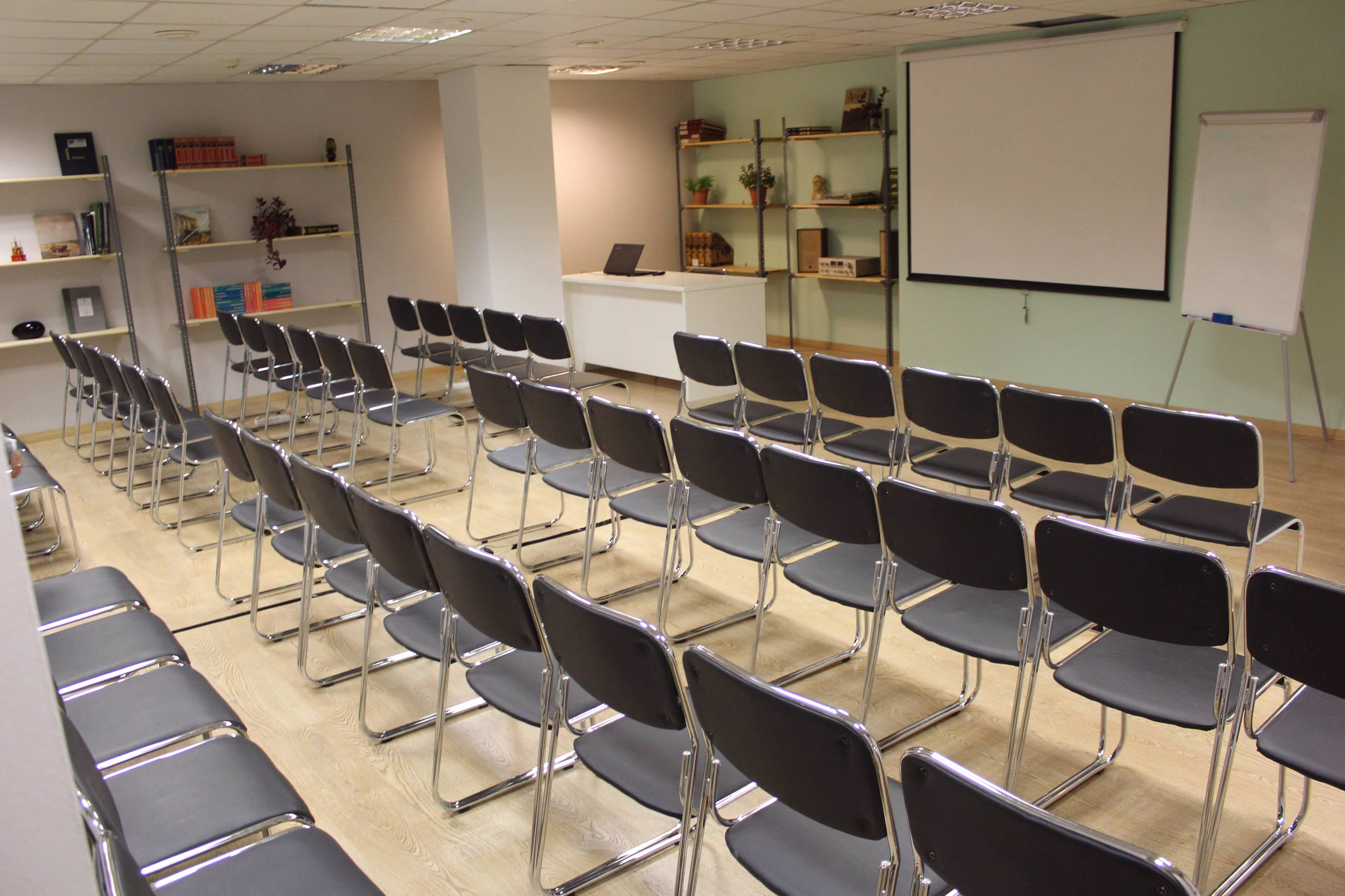 Conference room with theater-style rows of chairs facing a screen, whiteboard, flipchart