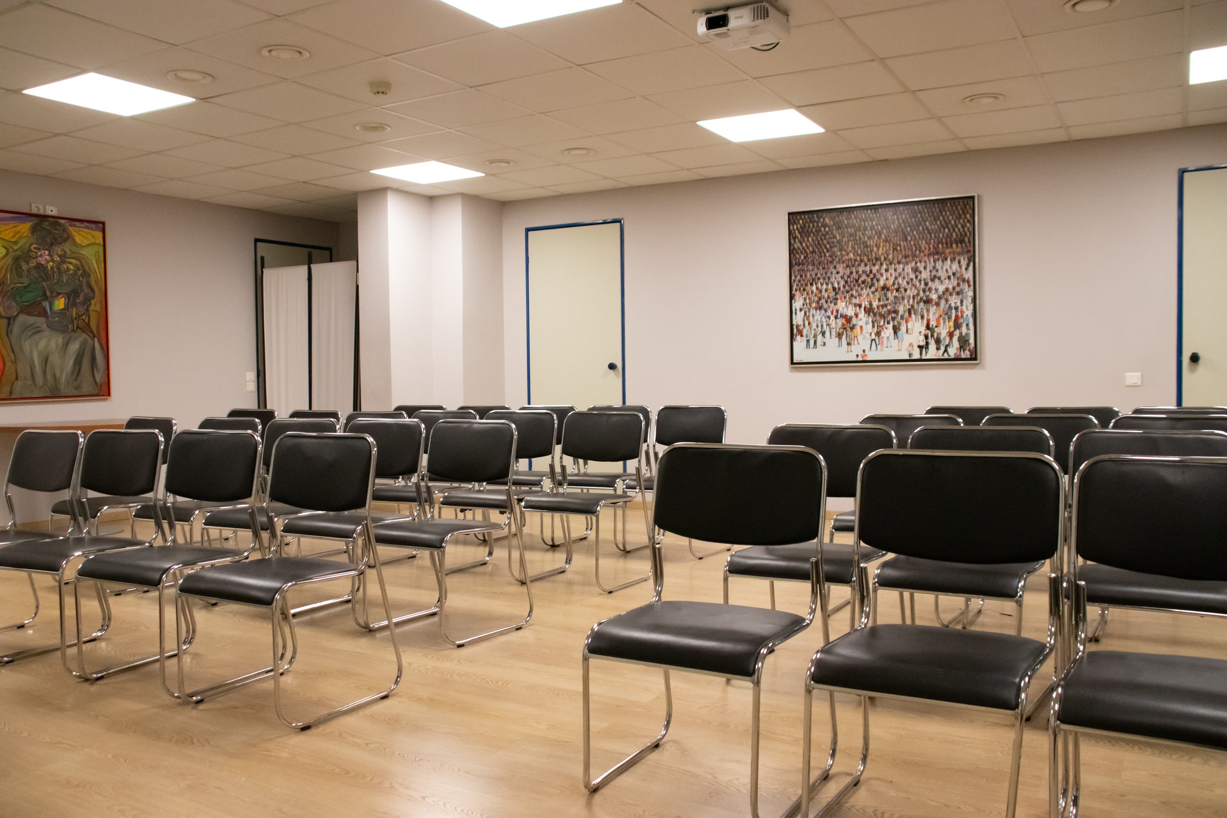 Meeting room with theater-style chair setup, light-colored walls, and paintings on the wall.