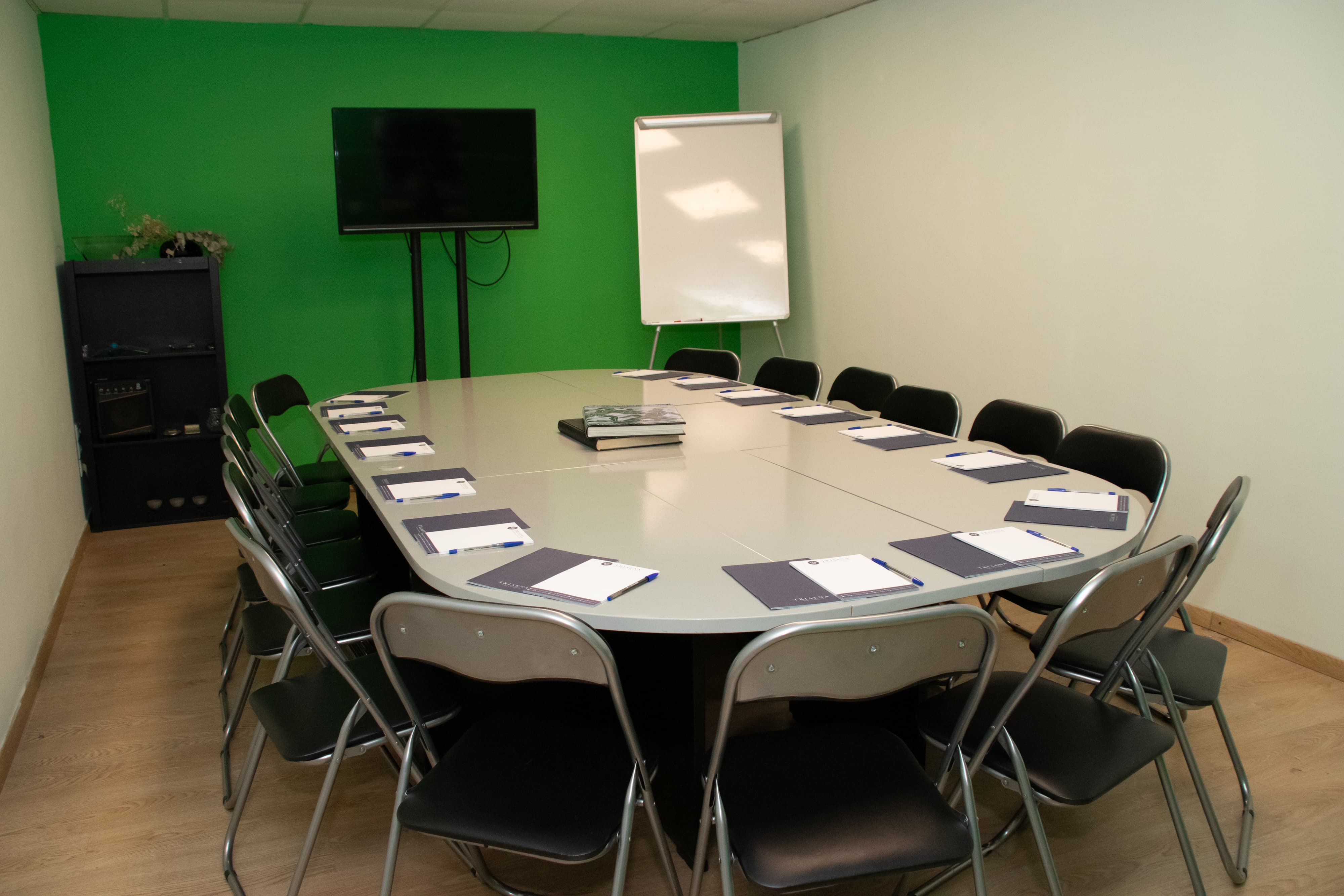 A meeting room with a green-painted wall and an oval-shaped table surrounded by chairs.