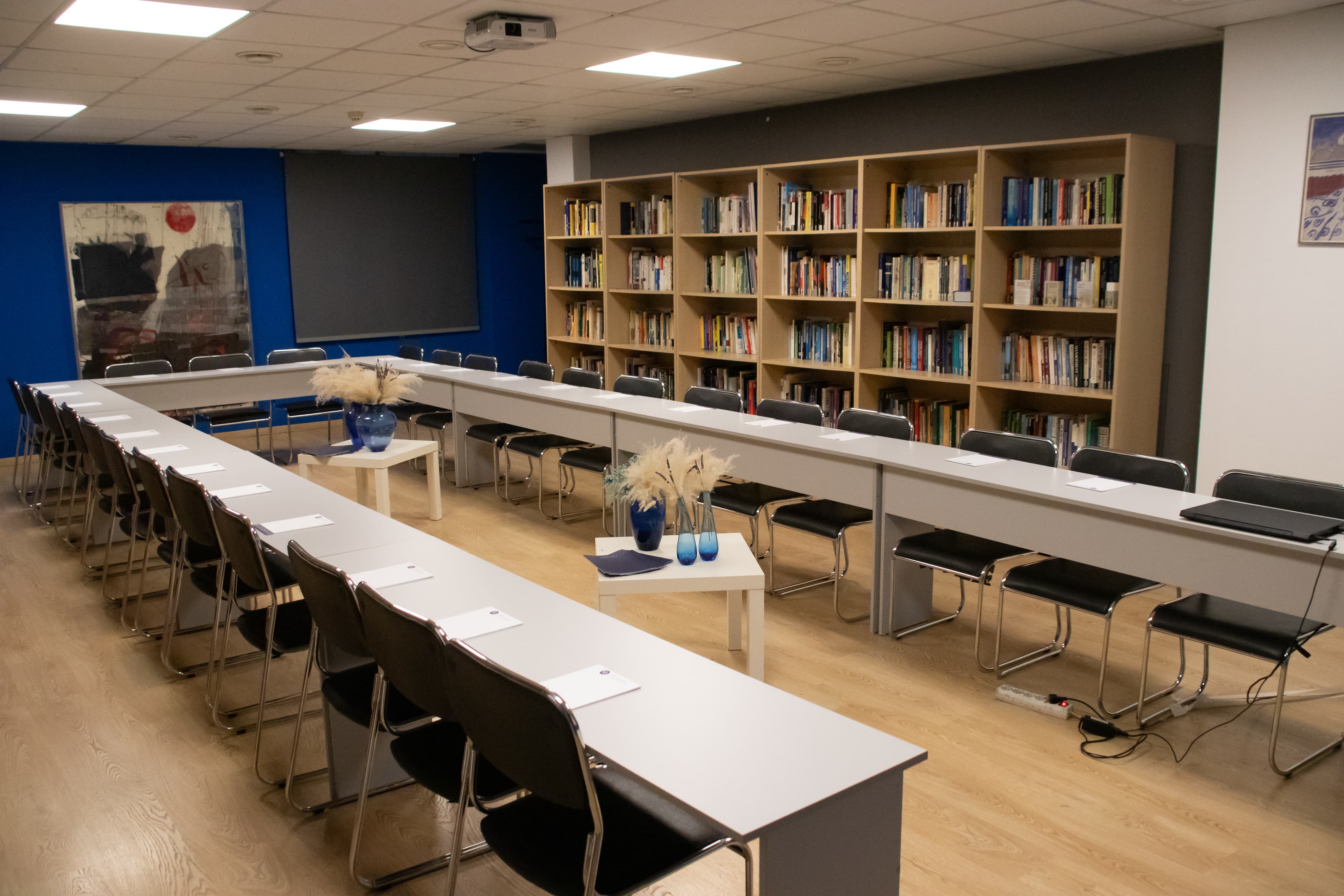 Meeting room with U-shaped table arrangement, chairs on the outer side, and bookshelves along the wall.