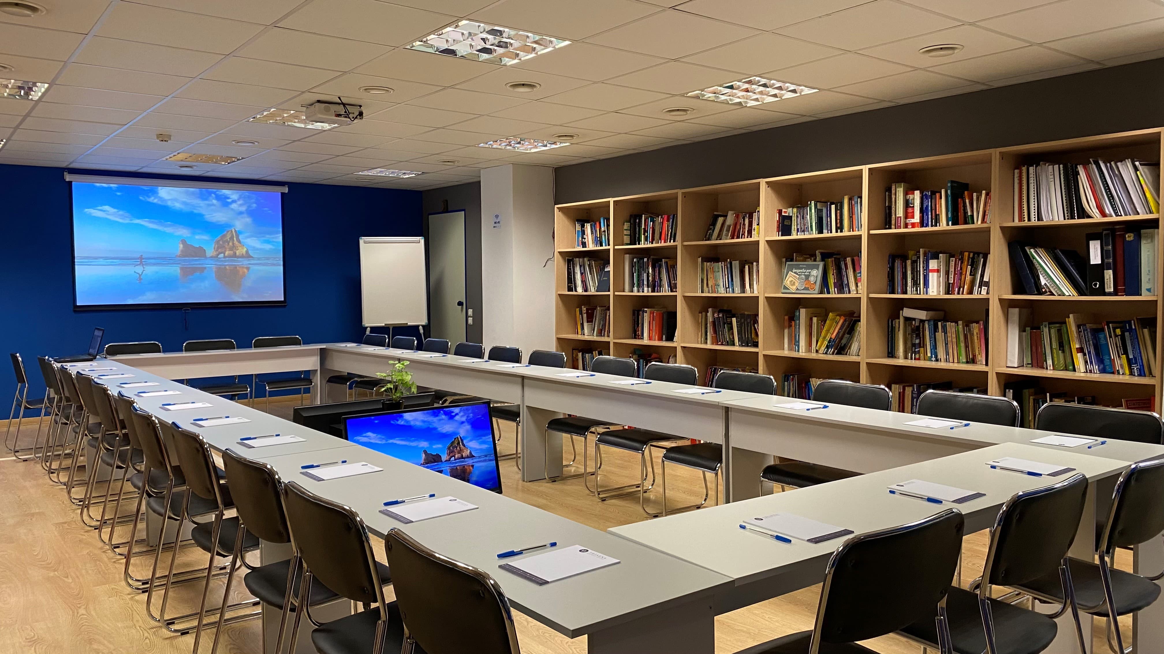 Large meeting space with O-shaped tables, presentation screen, and bookshelves along the walls.