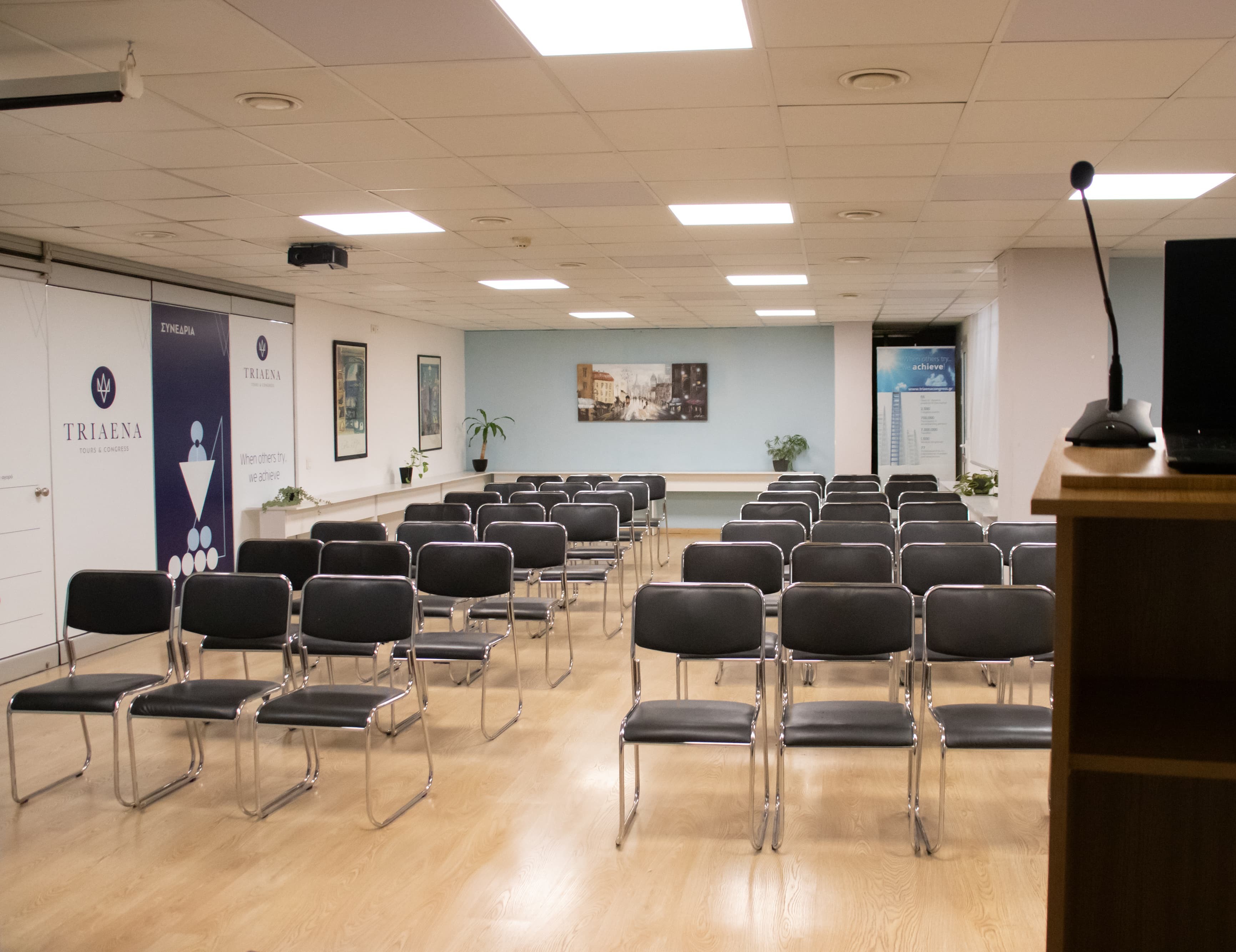 TRIAENA Business Center seminar room prepared for a professional presentation. conference room with rows of black chairs facing a podium with a microphone, set up for a presentation or seminar.