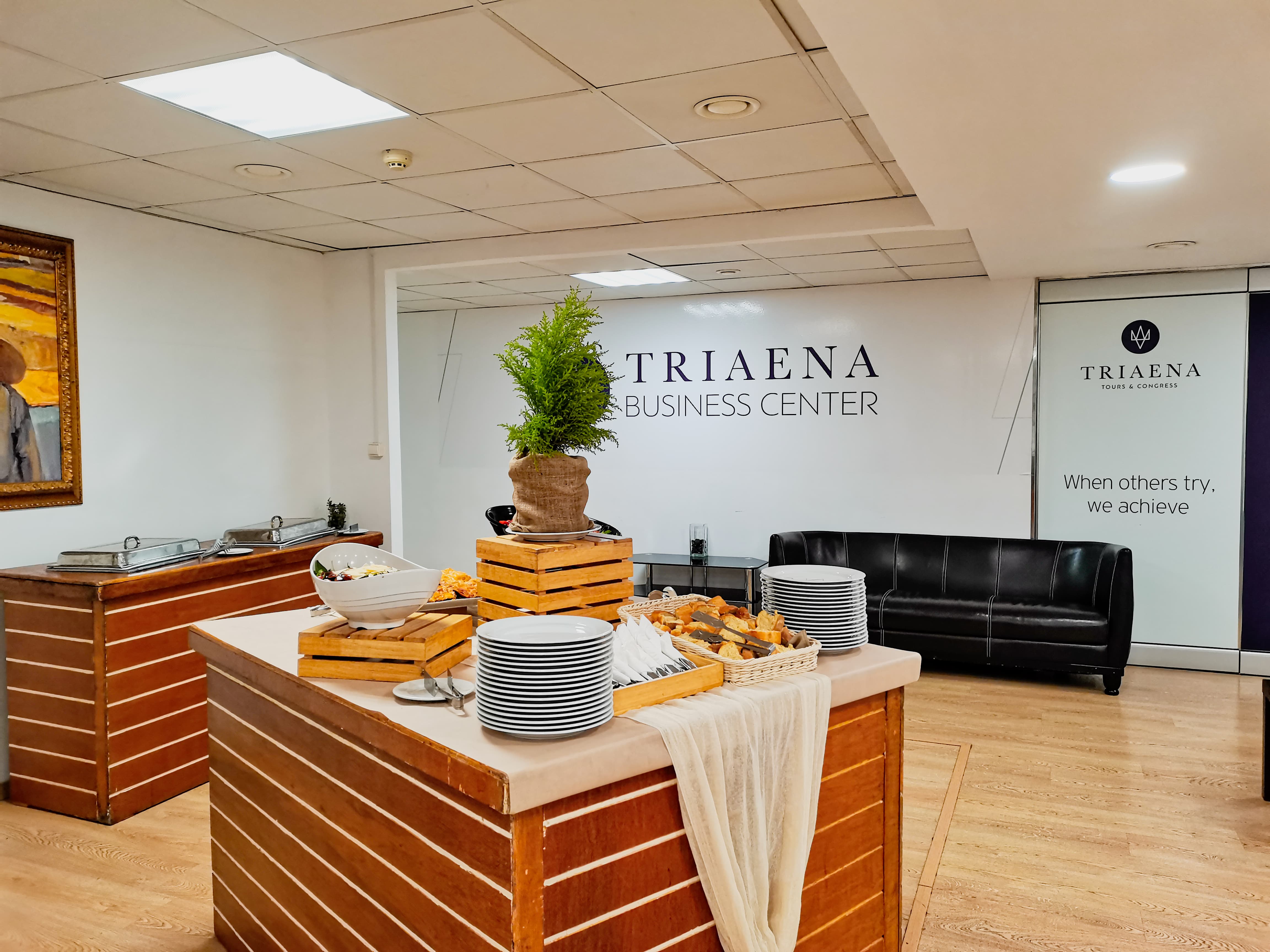 Triaena Business Center light lunch set up with catering buffet, black leather couches for seating area, painting, plates, food. When others try, we achieve