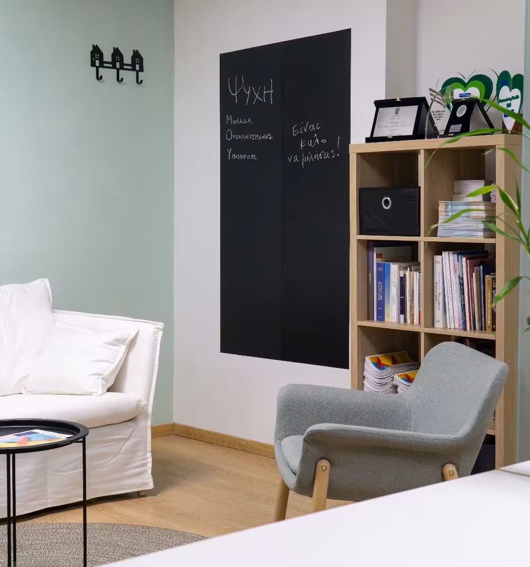 Modern office lounge area with white sofa, gray armchair, round rug, bookshelf filled with books, a black chalkboard wall for handwritten notes. Relaxed office modern seating designed for creativity and collaboration.
